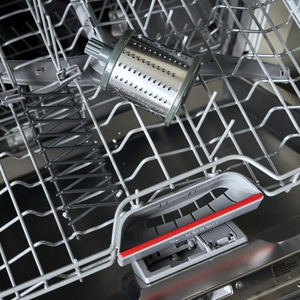 Open dishwasher with an empty rack, a Zyliss Fine Grating Drum placed inside—crafted from stainless steel—and the detergent compartment open and empty.