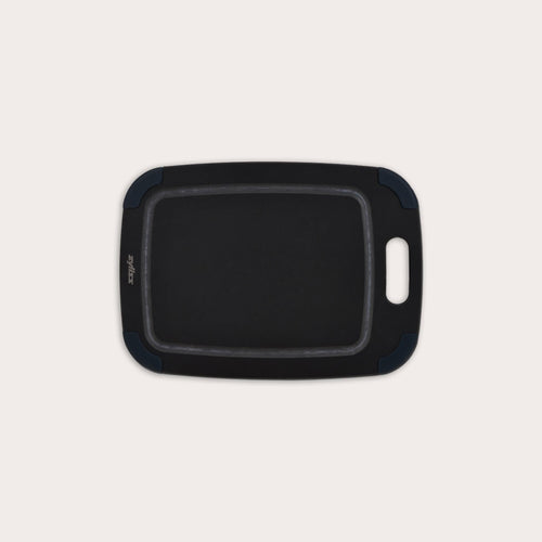 The Zyliss Wood Fibre Cutting Board is rectangular with rounded edges, a built-in handle, and dark blue corner grips. Made from recycled wood fibres, it is shown on a plain light background. #Small