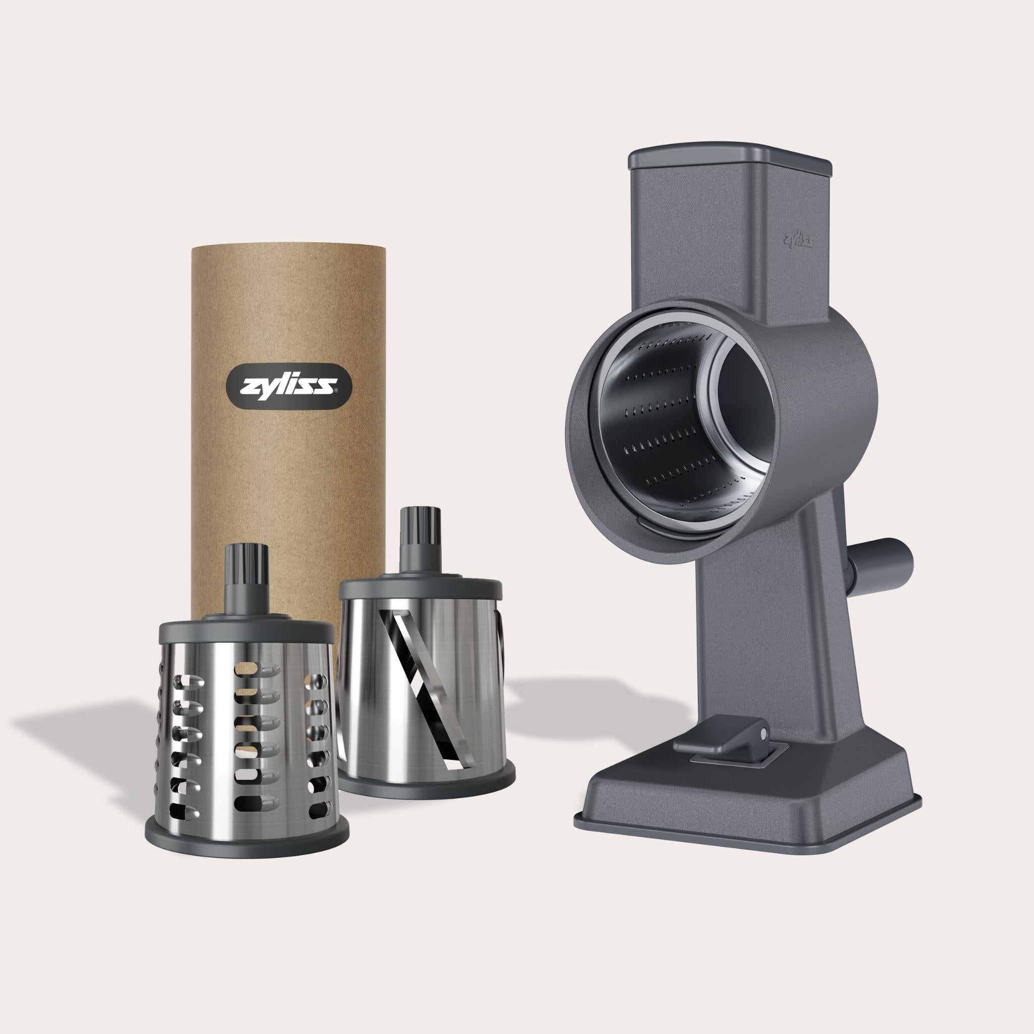 #drumgraterset The Zyliss Gourmet Drum Grater, made of gray stainless steel with a hand crank and two interchangeable blades, comes in a brown cardboard tube labeled Zyliss and is shown on a white background.