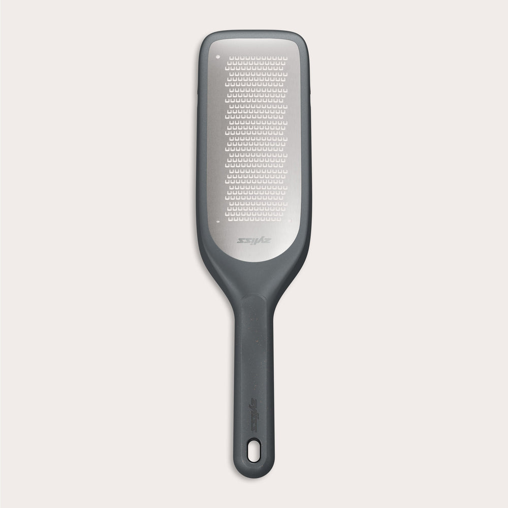 The Zyliss Fine Grater features a black and silver design with a rectangular ultra-sharp grating surface and a handle with an end hole, displayed on a plain light background. 