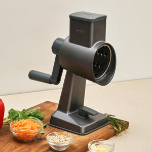 #drumgratersingle The Zyliss Gourmet Drum Grater sits on a kitchen counter beside a board with grated carrots and bowls of cheese and herbs—a stainless steel grater designed for effortless meal prep.