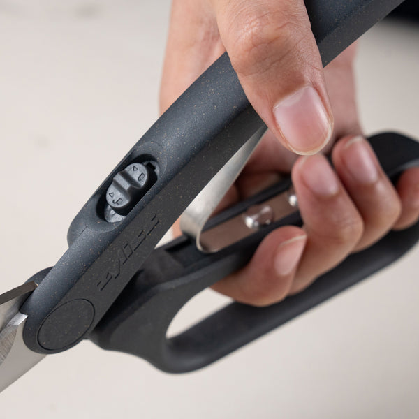 A hand holds Zyliss All Purpose Shears with ergonomic handles, highlighting the numbered adjustment dial on the handle for customized tension.