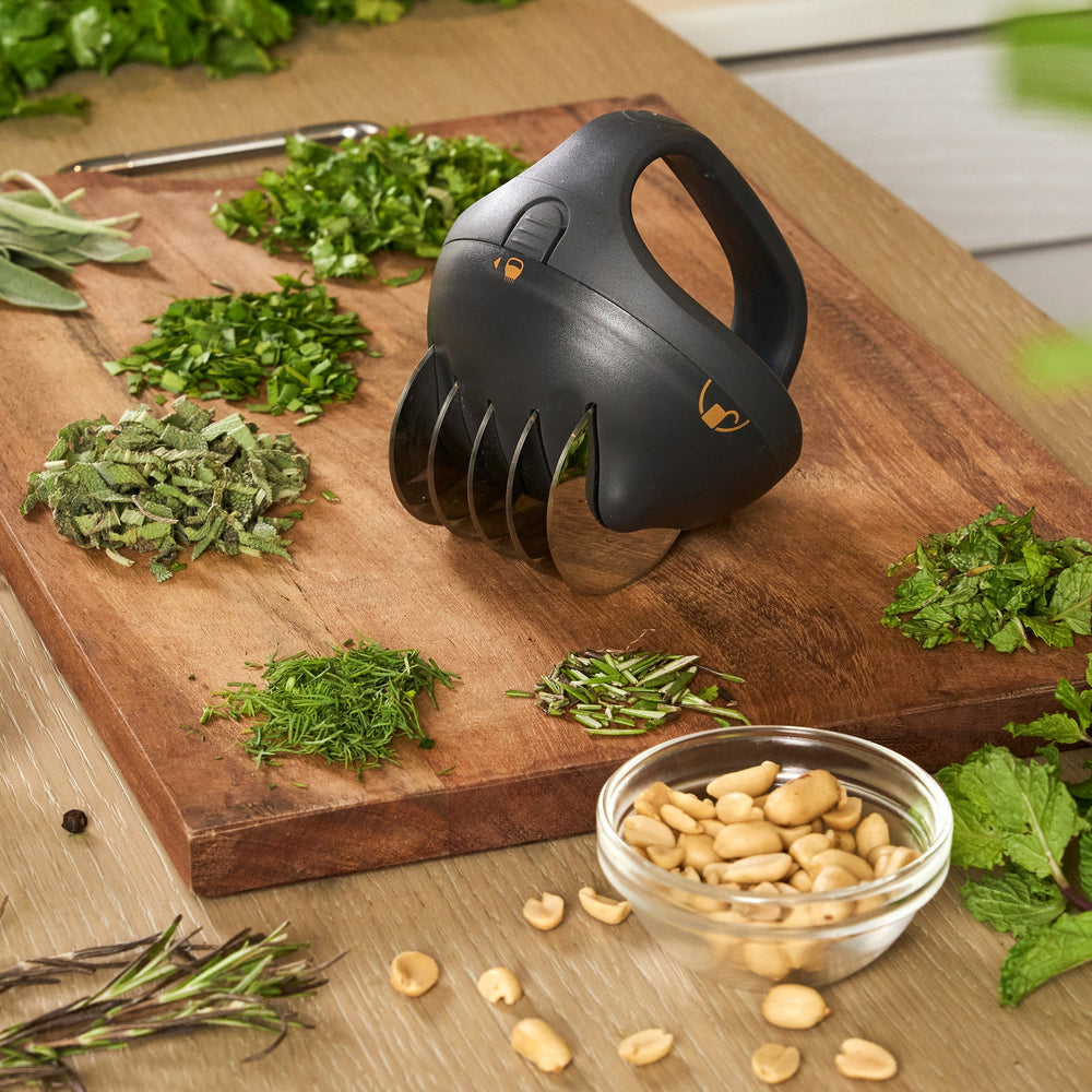 The Zyliss Fast Cut Herb Tool is a black handheld chopper with an ergonomic handle and clear stainless steel blades, perfect for slicing or chopping herbs, shown isolated on a light background.
