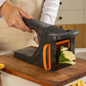 A person uses the Zyliss Potato & Vegetable Chipper with stainless steel blades and an orange handle to cut zucchini into uniform sticks on a wooden cutting board in the kitchen.