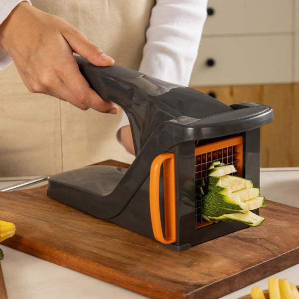 A person uses the Zyliss Potato & Vegetable Chipper with stainless steel blades and an orange handle to cut zucchini into uniform sticks on a wooden cutting board in the kitchen.
