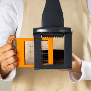 A person in a beige apron holds a Zyliss Potato & Vegetable Chipper with stainless steel grid blades, ready for slicing.