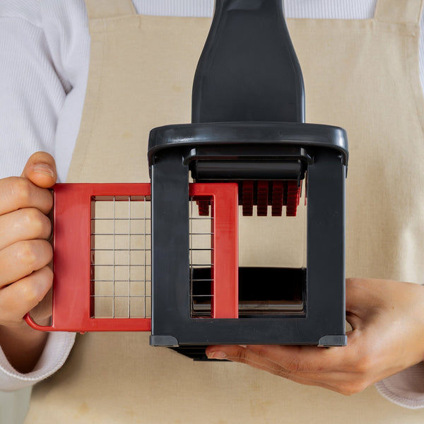 A person in a beige apron holds the Zyliss Potato & Vegetable Chipper, featuring stainless steel blades and a grid design, ready for use against a neutral background.