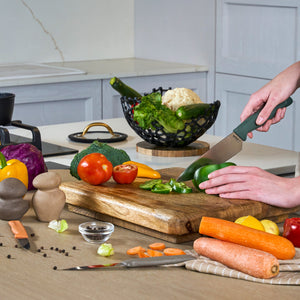 In a modern kitchen, someone uses the Zyliss 3 Piece Knife Set to slice a green bell pepper on a wooden cutting board surrounded by fresh tomatoes, carrots, broccoli, and yellow peppers.