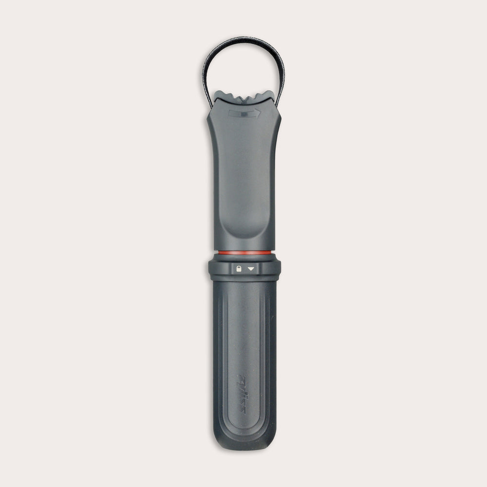 The Zyliss Jar Opener, shown vertically against a light background, is a black and gray handheld tool with a textured grip, integrated locking mechanism, circular top loop, and comes with a protective blade sheath. 