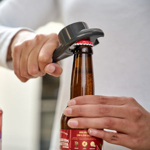 A person in a white shirt uses the Zyliss 5 In 1 Opener, featuring a quirky denture-shaped design with red gums and white teeth, to open a glass bottle. They enjoy its ergonomic grip and unique style.