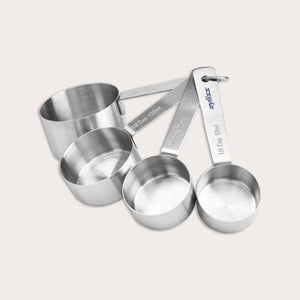 The Zyliss Stainless Steel Measuring Cups set includes four stacked, fanned-out cups, each labeled in cups and milliliters for precise ingredient measurement. 