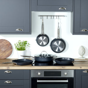 Modern kitchen with dark grey cabinets, wooden countertop, cast iron pans on the stove, a Zyliss Ultimate Pro Non-Stick Square Grill Pan With Pouring Lip hanging on a rack, a plant in a white pot, wooden board, and decorative artichoke sculpture. 