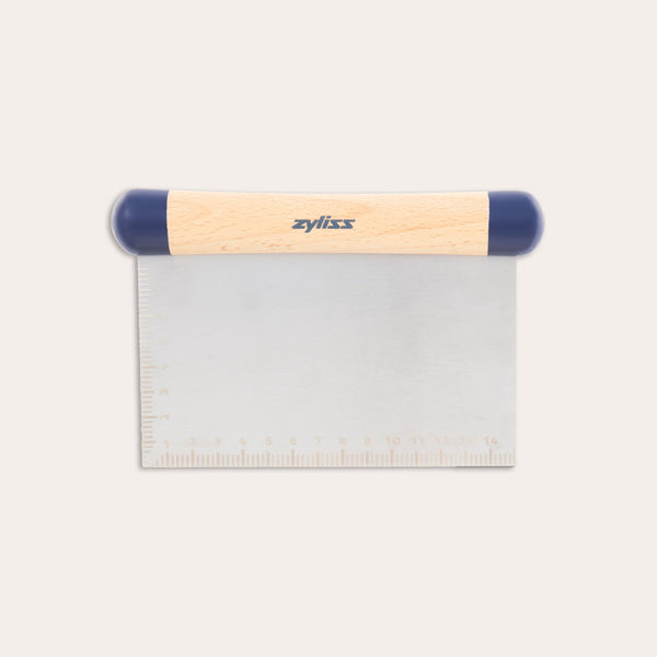 The Zyliss Beech Wood Bench Scraper features a beech wood handle, blue plastic ends, and a metal blade with an etched ruler—a versatile tool for baking tasks. 