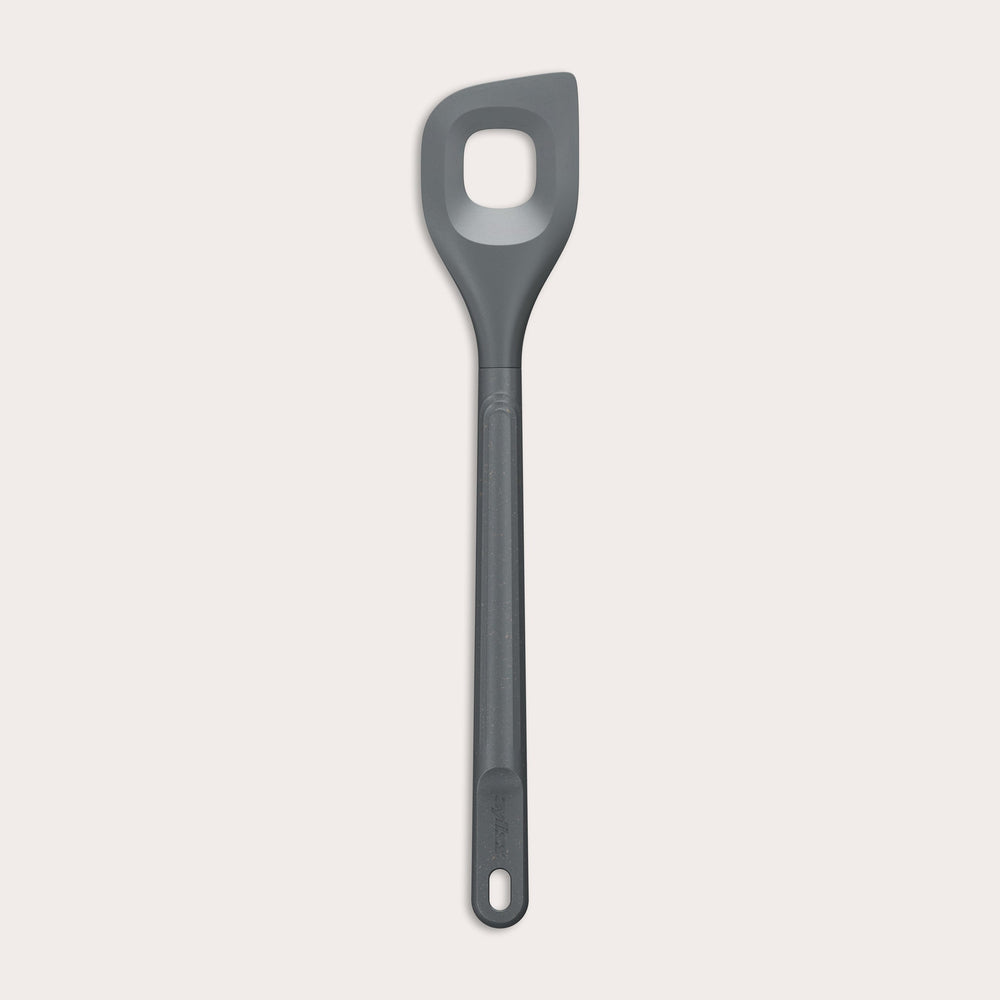 The Zyliss Angled Mixing Spoon is a gray silicone utensil with an ergonomic handle and a rectangular hole in the head, designed for non-stick cookware. Shown on a plain white background. 