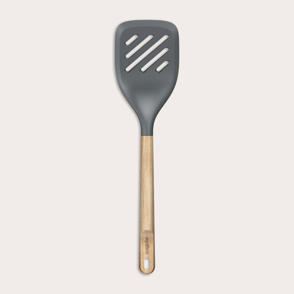 The Zyliss Oak Wood Slotted Turner is a kitchen essential with a wide, dark gray head and light oak wood handle, shown on a plain white background.