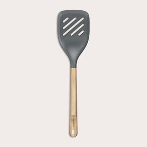The Zyliss Oak Wood Slotted Turner is a kitchen essential with a wide, dark gray head and light oak wood handle, shown on a plain white background.