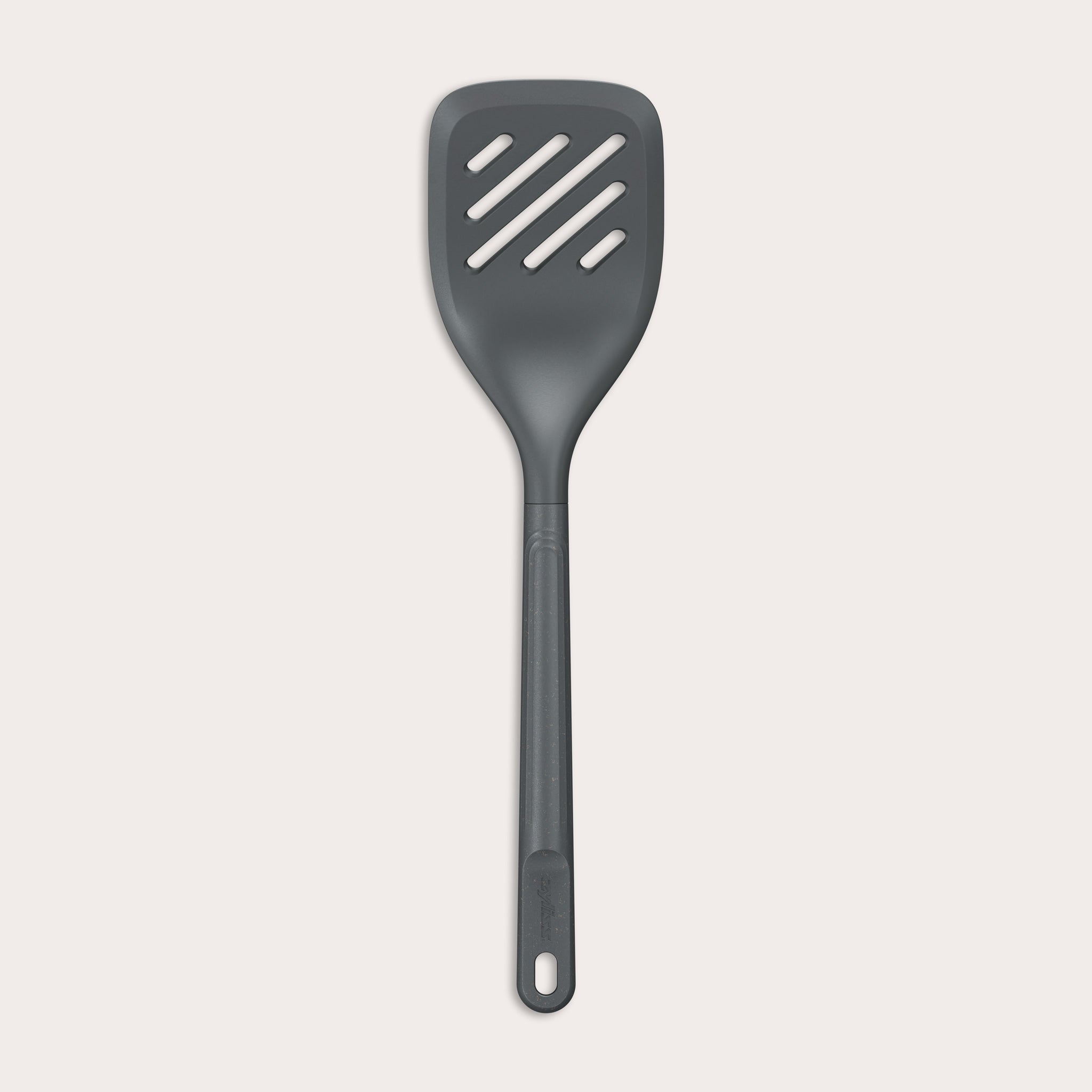 The Zyliss Slotted Turner, shown in black with three diagonal slots and an ergonomic handle, features a heat-resistant design for safe cooking or flipping food. Displayed against a plain white background. 