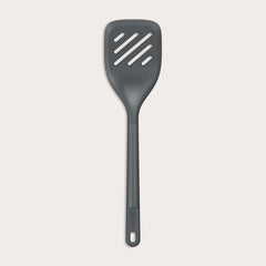 The Zyliss Slotted Turner, shown in black with three diagonal slots and an ergonomic handle, features a heat-resistant design for safe cooking or flipping food. Displayed against a plain white background. 