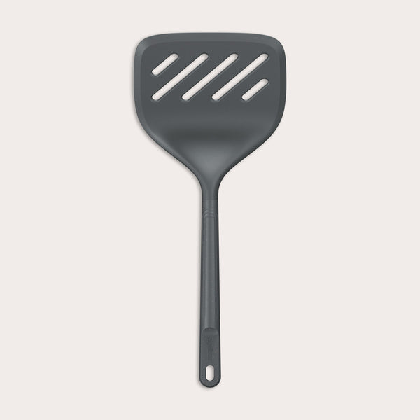 A Zyliss Turner XL slotted spatula in black, featuring a wide square head with three diagonal slots, ergonomic handle, and heat-resistant design is displayed against a plain light background. 