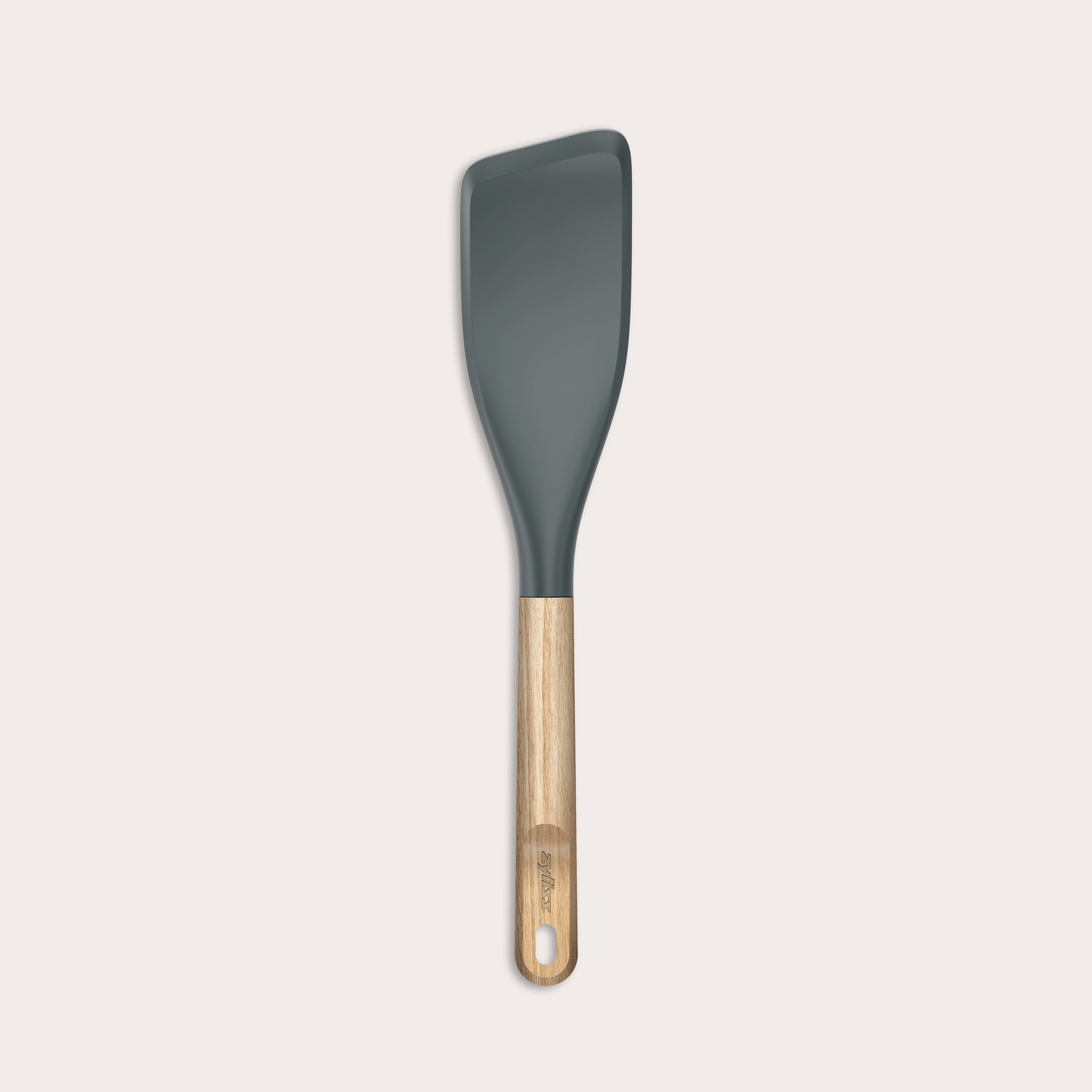 The Zyliss Oak Wood Easy Lift Turner has a dark gray silicone head, an oak wood handle, and a hanging hole at the end. It is shown on a plain light background.