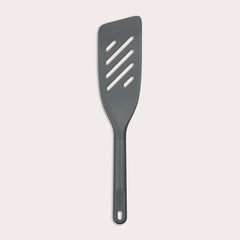 The Zyliss Fish Turner is a dark gray, heat-resistant slotted spatula with an angled edge and a handle featuring a hole at the end, displayed on a plain white background. 