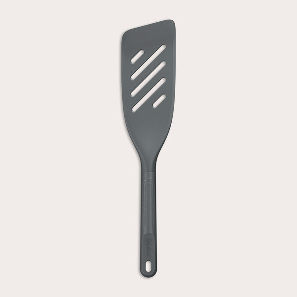 The Zyliss Fish Turner is a dark gray, heat-resistant slotted spatula with an angled edge and a handle featuring a hole at the end, displayed on a plain white background. 