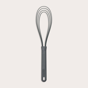 The Zyliss Flat Whisk Silicone features a black, heat-resistant silicone design with a long handle and looped wires, displayed on a plain light background. 