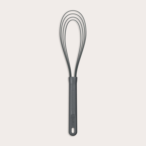 The Zyliss Flat Whisk Silicone features a black, heat-resistant silicone design with a long handle and looped wires, displayed on a plain light background. 