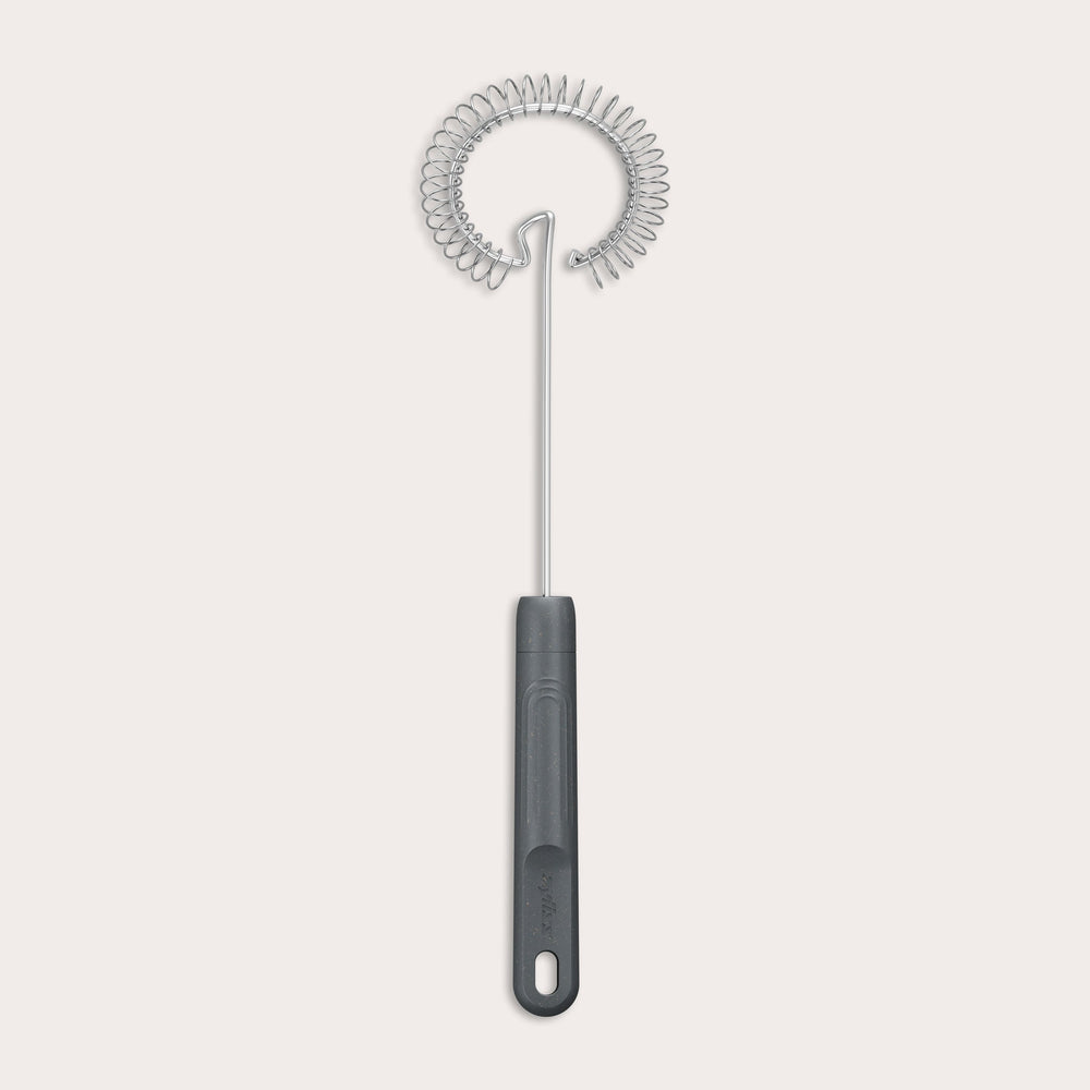 The Zyliss Gravy Whisk features a metal spiral and a dark plastic handle with a hanging hole. It is heat-resistant and shown against a plain light background. 
