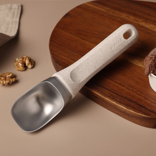 #naturalbeige A Zyliss Ice Cream Scoop with an eco-friendly handle sits on a round wooden board, surrounded by walnuts, with a bowl of chocolate ice cream partially visible.