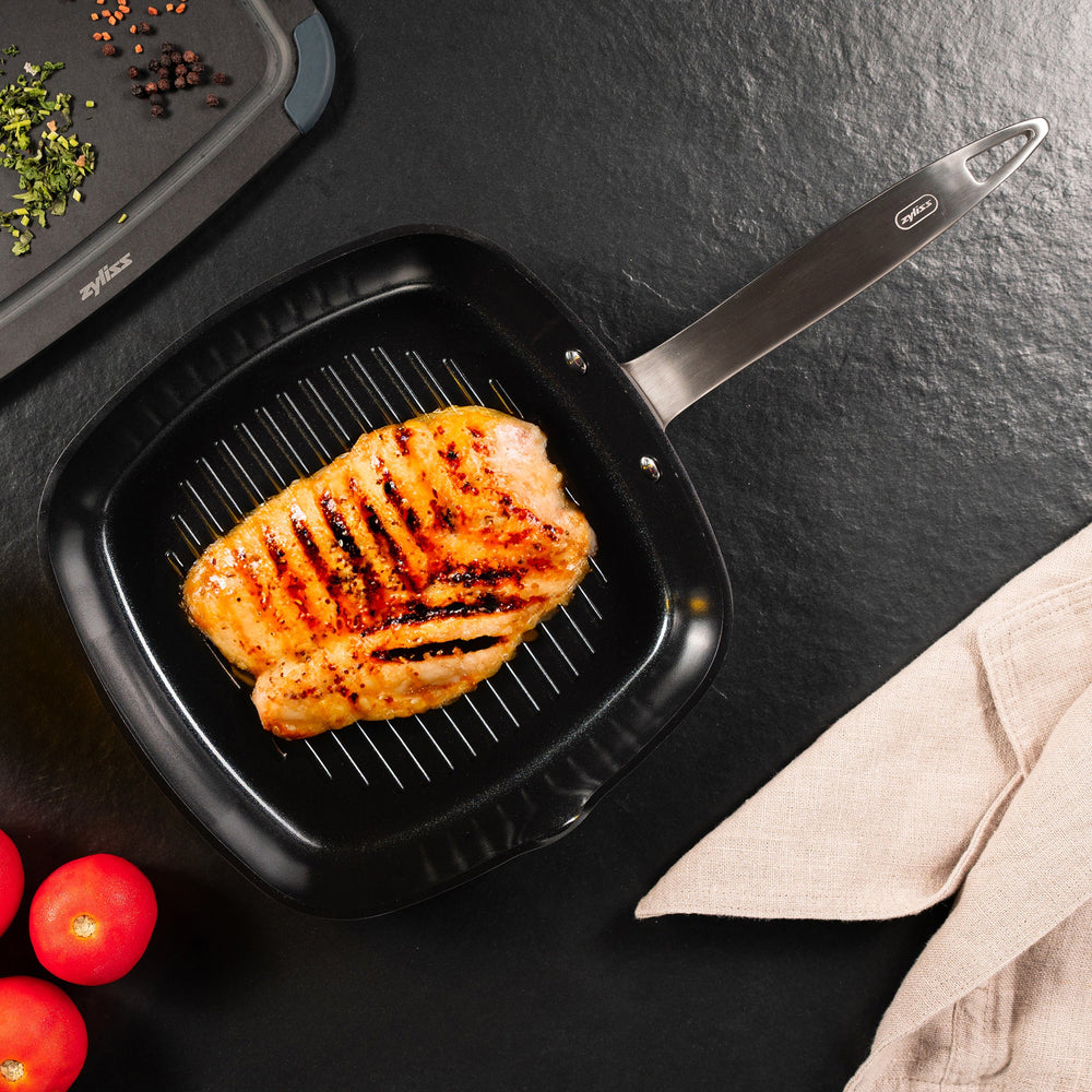 The Zyliss Ultimate Pro Ceramic Square Grill Pan is black with ridges, a silver handle, and a durable non-stick coating—ideal for indoor grilling. Displayed against a plain light background. 