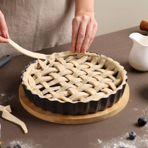 Someone weaves pie dough strips into a lattice over dark berries in the Zyliss Non-Stick Tart Pan with removable base, which sits on a wooden board on a brown table.