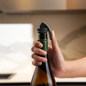 A hand presses a wine bottle onto the Zyliss Bottle Stopper 2 Piece Set in a kitchen, showing efficient drink storage with the black reusable stopper attached to the bottle’s neck.
