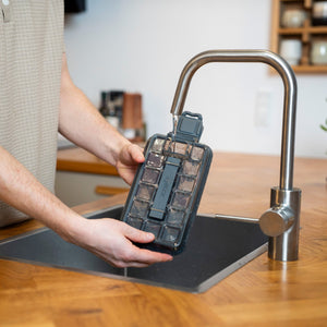 A person fills the Zyliss Press & Pull Ice Cube Tray with water under a faucet in a modern kitchen with wooden countertops.