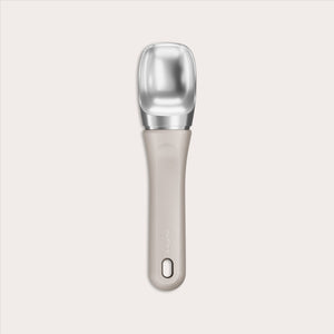 #naturalbeige The Zyliss Ice Cream Scoop features a wide, flat silver scoop and an eco-friendly beige handle made from sustainable wheat straw, with a small hole near the end, shown centered on a plain light background.