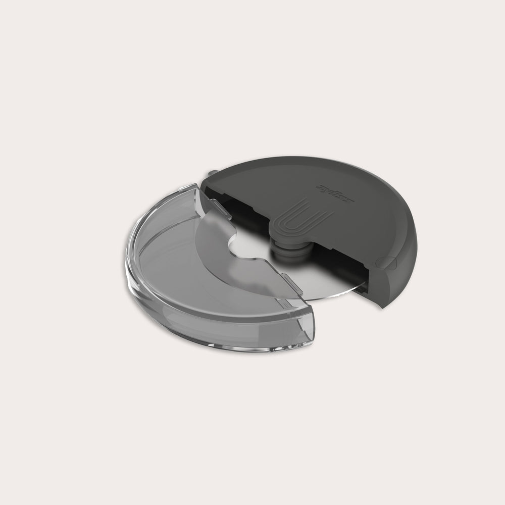 The Zyliss Pizza Wheel sits against a plain light background in a round black and transparent plastic case with a partially open sliding cover, revealing its ergonomic handle and stainless steel blade inside.