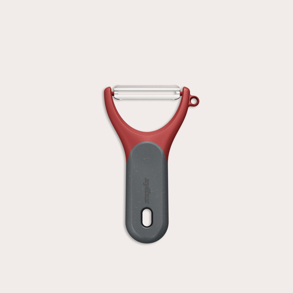 The Zyliss Soft Skin Y Peeler, shown against a white background, features a red and gray ergonomic grip, wide handle, and stainless steel blade for eco-friendly peeling. 