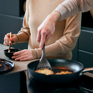 Two people in neutral long sleeves cook together: one stirs in a small bowl with the Zyliss 5-Piece Utensil Set, while the other uses a spatula at the stove. Both enjoy these dishwasher safe kitchen tools. 